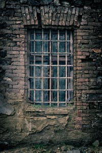 A moody close-up of an old brick wall featuring a barred window, capturing a sense of nostalgia.