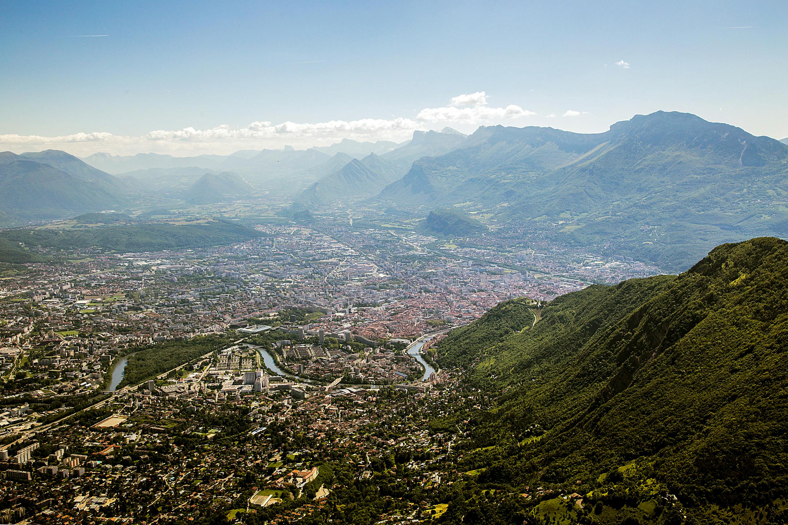 Breathtaking aerial view of Grenoble city with surrounding Alps mountains under a clear sky.